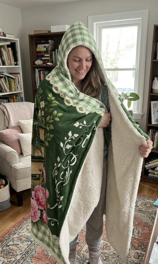 A woman wrapped in a green floral blanket with gingham trim and a cream lining