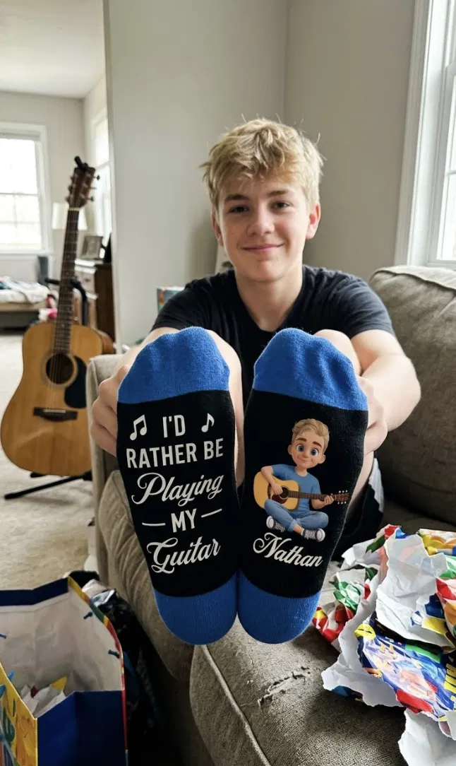 A young person showing blue guitar-themed socks personalized with the name Nathan